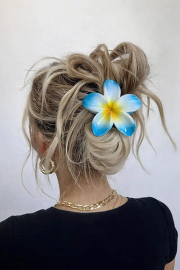 Person with blonde hair styled in an updo with a blue and yellow flower accessory against a white background